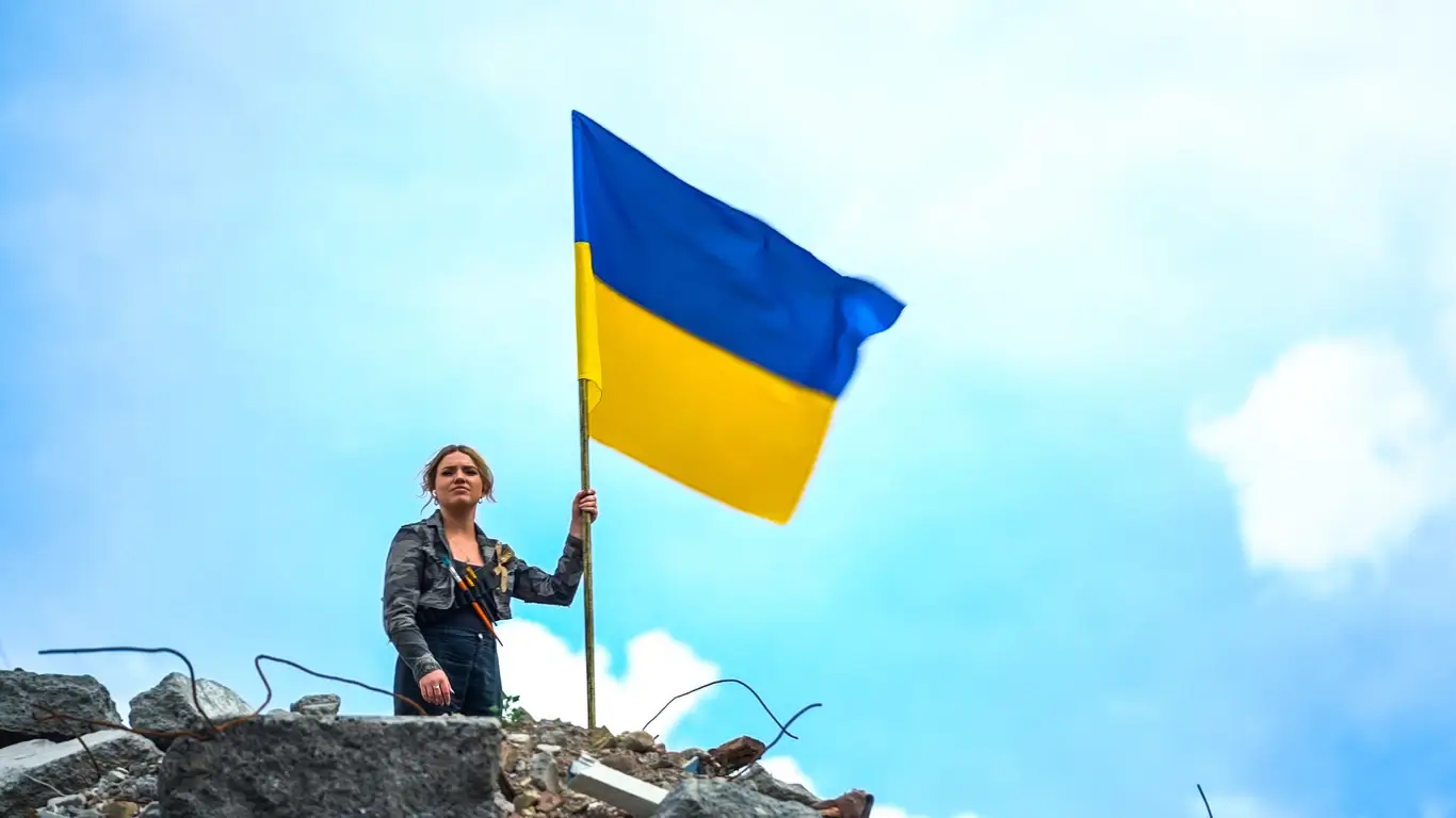 Kelsie Kimberlin stands amid the ruins holding a Ukrainian flag